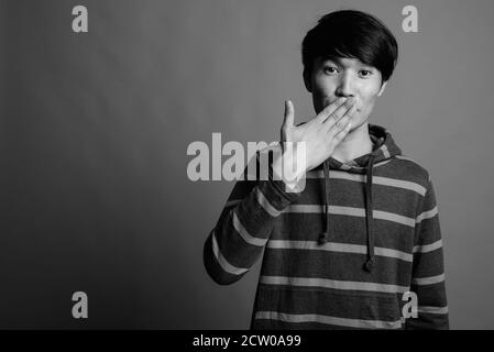 Young Asian man wearing striped hoodie against gray background Stock Photo