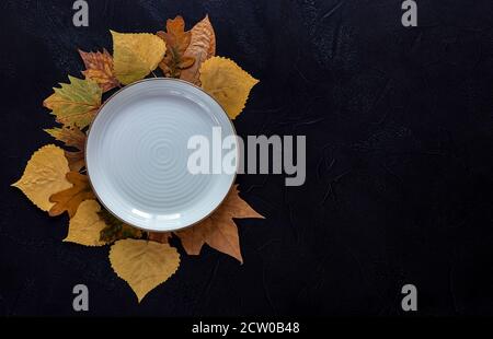 Autumn and Thanksgiving day table setting with fallen leaves and empty white plate on the dark background Stock Photo