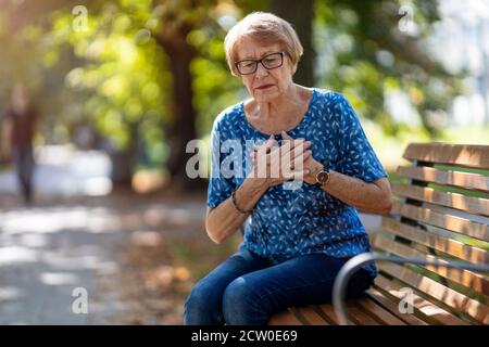 Senior Woman Suffering From Chest Pain While Sitting On Bench Stock Photo