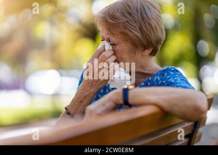 Unhappy senior woman wipes her eyes with a tissue outdoors Stock Photo
