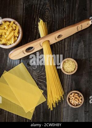Different types of pasta on dark wooden table. Spaghetti, lasagne, fusilli. Overhead shot. Stock Photo