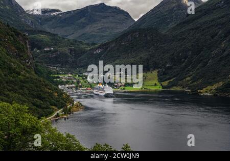 Geiranger fjord seen from the hillside on summer day with one cruise ship in port and the tall mountains behind, Norway Stock Photo