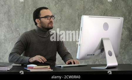 Angry man sitting at the table with computer over gray backgroun Stock Photo