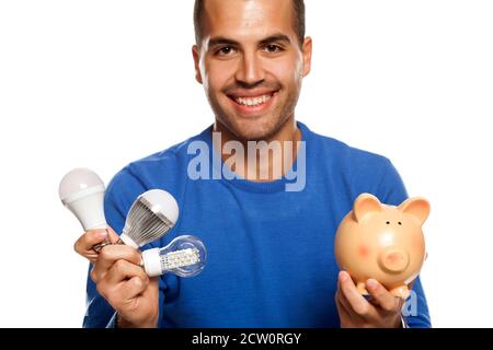 portrait of happy young man, holding three different LED bulbs and piggy bank on white background Stock Photo