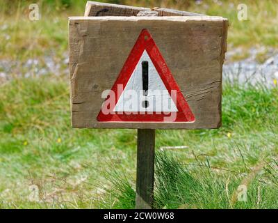 Warning road sign with an exclamation mark in red triangle on mountain trial in summer. Stock Photo
