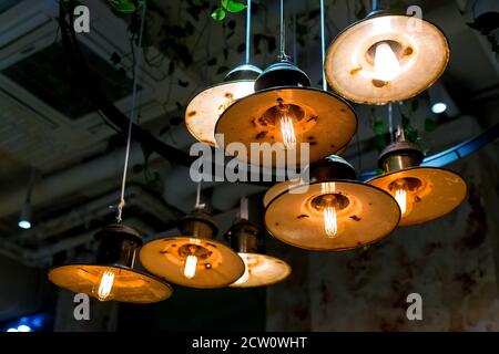 several round pendant retro loft style lanterns with edison bulbs shine with warm light in the interior of a dark restaurant, close-up of hanging lamp Stock Photo