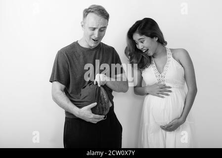 Happy young multi ethnic married couple with man opening shirt while using watermelon as pregnant stomach Stock Photo