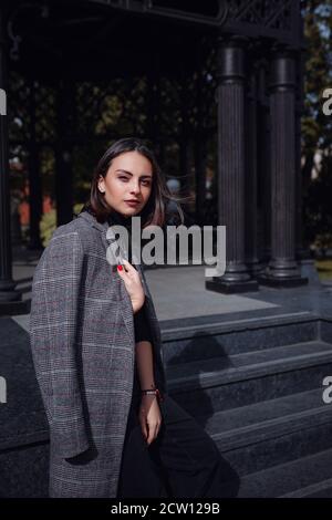 Beautiful young brunette woman walks in Moscow. Outdoors fashion portrait of stunning trendy woman posing on the street. Stock Photo
