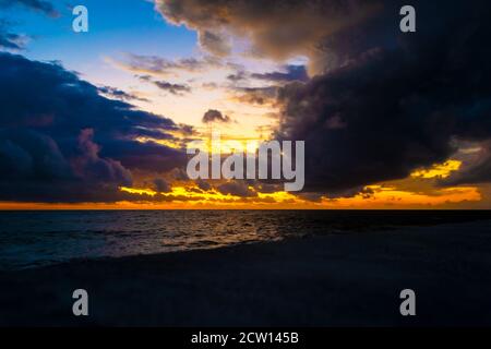 Dramatic sunset through a cloudy dark sky over waves at the sea. Stock Photo