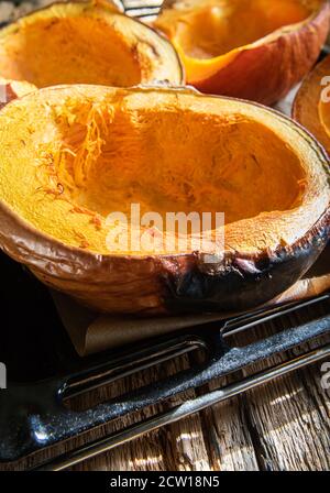 Close-up of halves of homemade freshly baked bright orange pumpkins on baking sheet and on oven tray and on natural textured wooden table surface. Rus Stock Photo