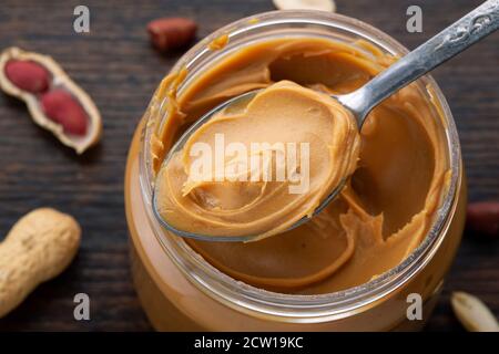 peanut paste in an open jar and peanuts in the peel scattered on the table Stock Photo
