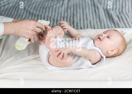 Mother puts socks on the baby. The baby is lying on the changing table and smiling. Motherhood Stock Photo