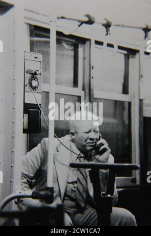 Fine 1970s vintage black and white photography of an older man talking on the public pay phone landline. Stock Photo