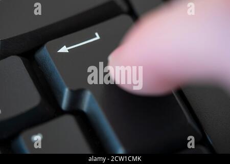 A man's finger hitting the return (enter) key on a computer keyboard. Concept: enter, ok, okay, return, go ahead, permission, technology, computing Stock Photo