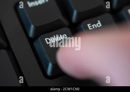 A macro closeup of a finger pushing the delete button on a computer keyboard. Concept: delete, remove, cancel, erase, cancel culture, deleted Stock Photo