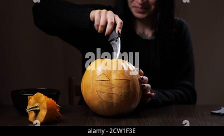 Young brunette woman carves a pumpkin for Halloween Preparation Stock Photo