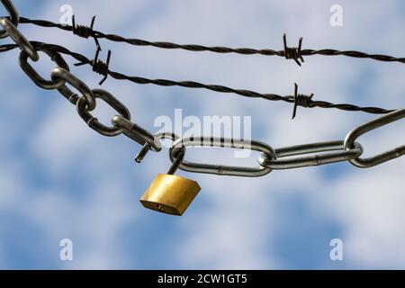 Padlock and steel chains with barbed wire against blue clouded sky symbolizing lockdown Stock Photo