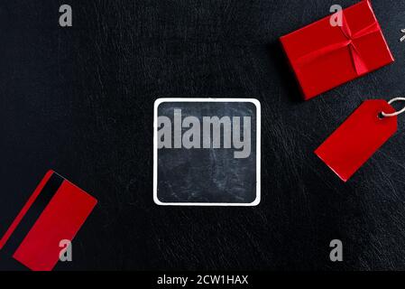 Creative backdrop with different things - sale tag, red present box, mock up credit card and square chalkboard on a black leather background, copy spa Stock Photo