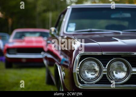 The headlights of vintage Chevrolet Malibu 1967 or 1969 are in focus and an old model Chevrolet Camaro is in the background. Stock Photo