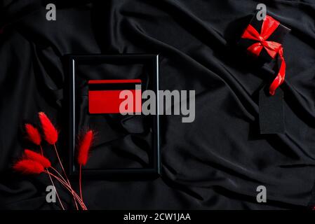 Decorative backdrop for Black Friday - mock-up credit or discount card, present box and dried natural red grass on a black silk tissue background, cop Stock Photo