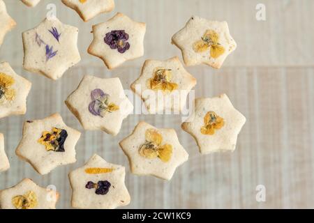 Star shaped biscuits decorated with edible flowers, pansies and cornflower petals. Photographed on a wooden background. Stock Photo