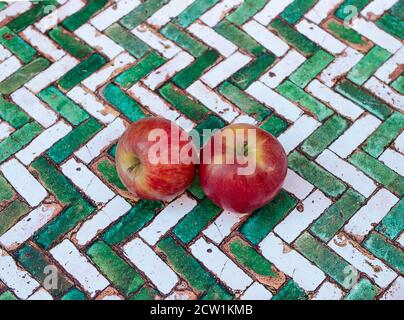 two organic red apples on green herringbone tiles. Top view Stock Photo