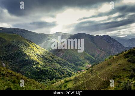 The sun's rays penetrate the clouds that threaten a storm, illuminating part of the mountain in the Somiedo Natural Park. Stock Photo