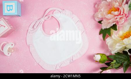 Baby bib nursery clothing mom bloggers desktop mockups with peonie floers on pink textured background. Top view blog hero header creative composition