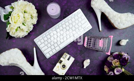 Wedding bridal theme desktop workspace with high heel shoes, bouquets and accessories, and shopping cart on vintage purple textured background. Top vi Stock Photo