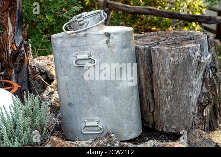 An old metal milk can, next to a large wooden log. Perfect shot to describe country life on a farm. Stock Photo