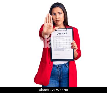 Young beautiful brunette woman holding clipboard with contract with open hand doing stop sign with serious and confident expression, defense gesture Stock Photo