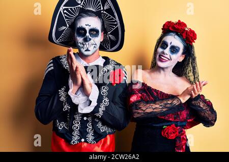 Young couple wearing mexican day of the dead costume over yellow clapping and applauding happy and joyful, smiling proud hands together Stock Photo