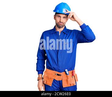 Young handsome man wearing worker uniform and hardhat shaking and freezing for winter cold with sad and shock expression on face Stock Photo