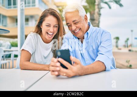 Middle age couple in love sitting at the terrace of coffee shop using smartphone happy and cheerful together Stock Photo