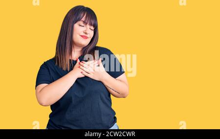 Young plus size woman wearing casual clothes smiling with hands on chest with closed eyes and grateful gesture on face. health concept. Stock Photo