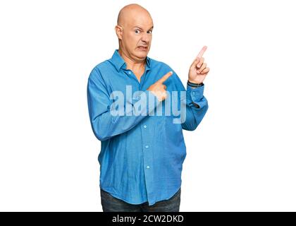 Middle age bald man wearing casual clothes pointing aside worried and nervous with both hands, concerned and surprised expression Stock Photo