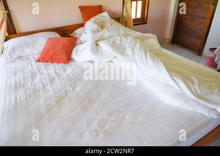 Unmade bed sheet of the crease and pillow white blanket in the bedroom after sleep on top view / Wrinkled fabric sunlight in the morning bed Stock Photo