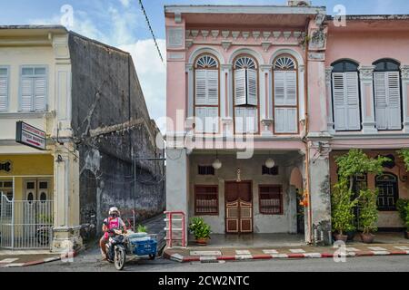 A man on a motorcycle with sidecar drives along the colorful old Sino-Portuguese shophouses in Krabi Rd. in the Old Town area of Phuket Town, Thailand Stock Photo