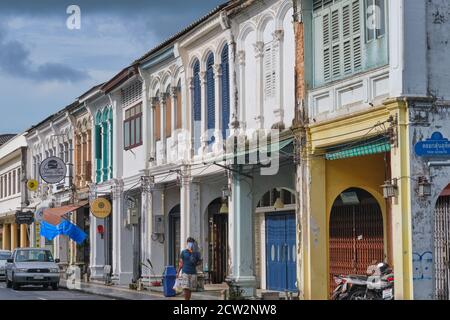 A man walks along a row of colorful Sino-Portuguese shophouses in Yaowarat Road in the Old Town (Chinatown) area of Phuket Town, Thailand Stock Photo
