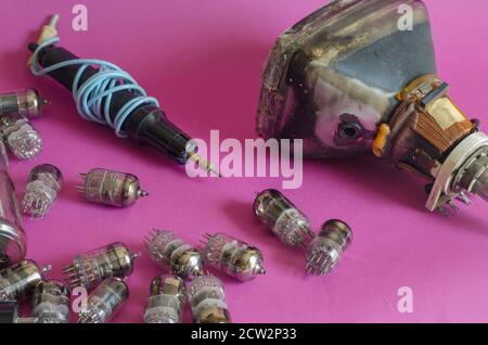 A group of random radio tubes, an induction soldering iron and an old picture tube on a pink background. Obsolete radio and television parts. Collecti Stock Photo