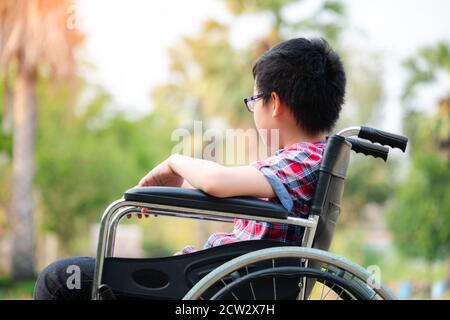 Alone young disabled man on wheelchair in the park, Patient is relaxing in garden decorations of the hospital feeling of missing someone, lonely Stock Photo