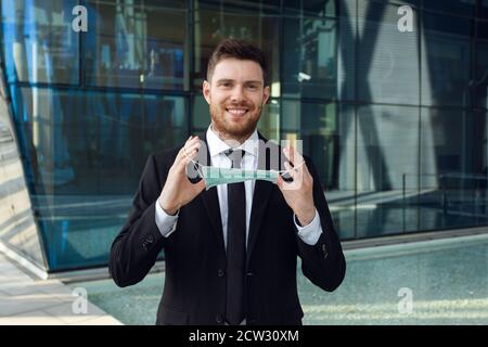 Businessman Puts on Medical Mask in Business Center. Business man in Black Suit. Healthy Concept Stock Photo