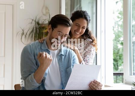 Excited couple triumph reading good news in paper letter Stock Photo