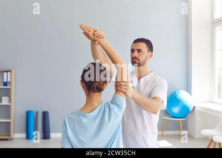 Young male osteopath masseur in white clothes kneads the joints of the girl's hand. Stock Photo
