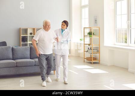 Healthcare worker helping senior man to walk in office of modern hospital or geriatric rehab center Stock Photo