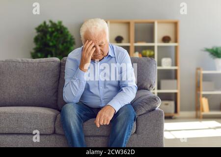 Depressed senior man sitting on sofa at home suffering from loneliness or bad headache Stock Photo