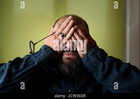 Man hides his face behind his hands so he doesn't have to see Stock Photo