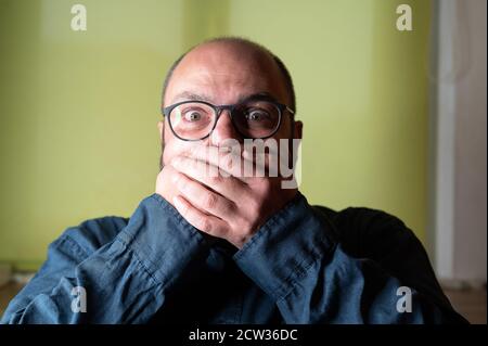 Man covers his mouth with both hands and looks scared into the camera Stock Photo
