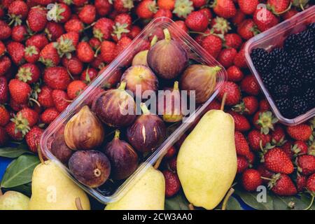 Purple figs, strawberries, blackberries and pears are standing at a grocery store stall. Stock Photo