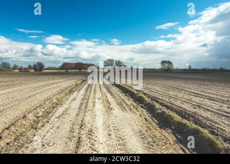 Dirt road through ploughed fields and clouds on the sky Stock Photo